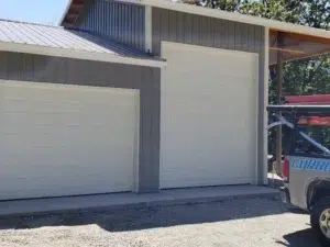 Two white sectional garage doors on a gray metal building with a garage door service truck parked outside in Snohomish